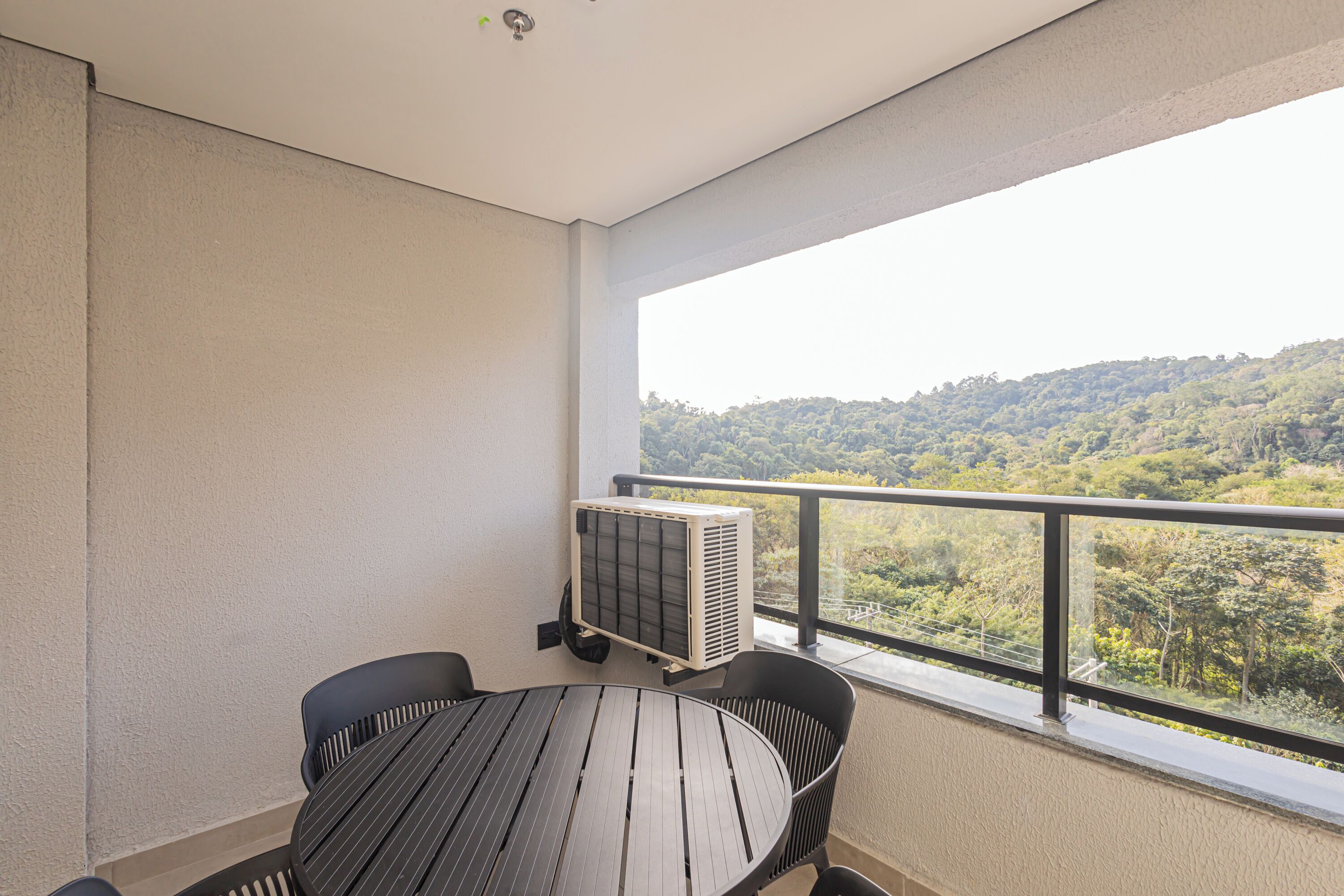 A balcony with a table and chairs, overlooking a forested hillside.