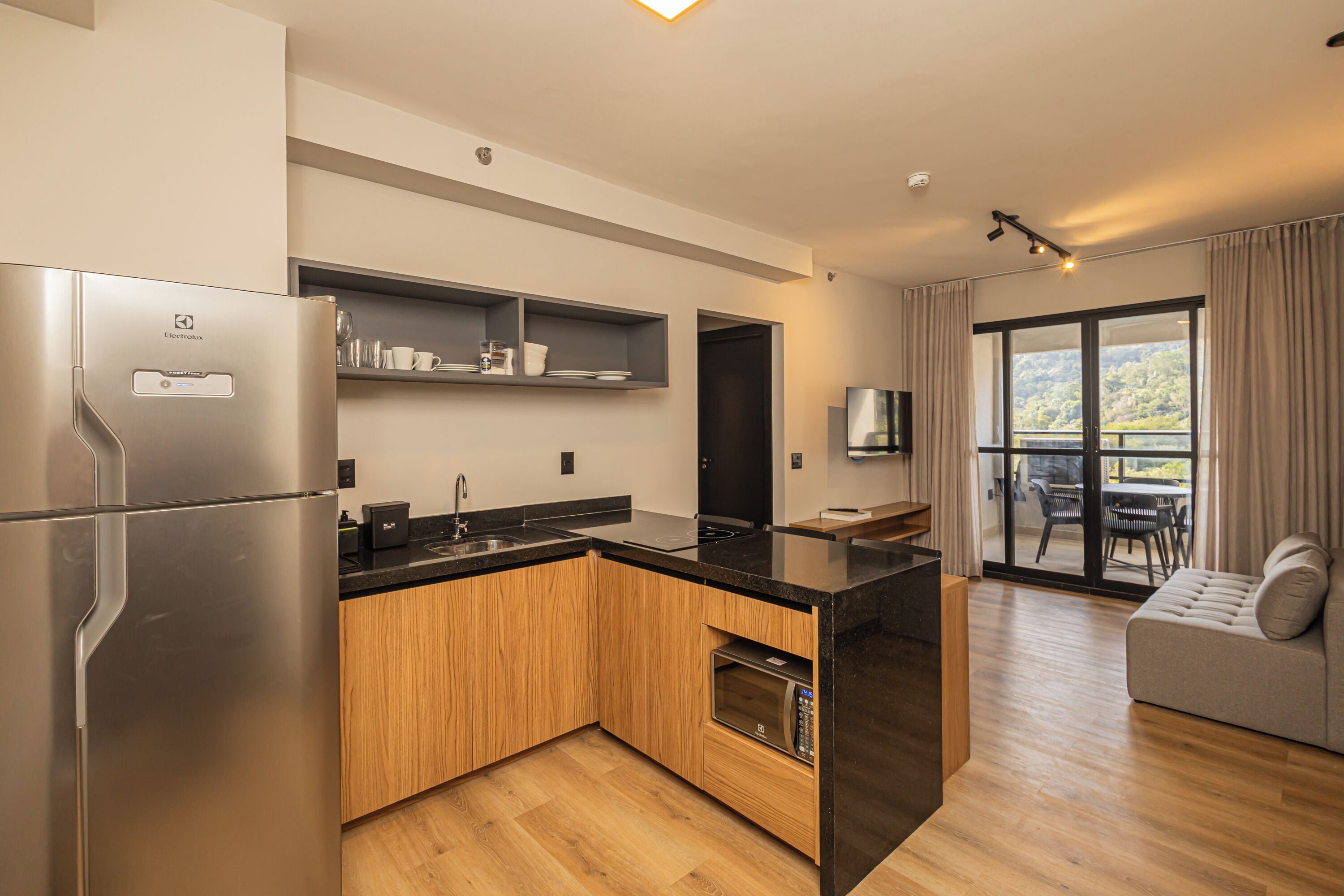 A modern kitchen with a built-in oven, a refrigerator, and a microwave. There is a dining area with a table and chairs, and a sofa.