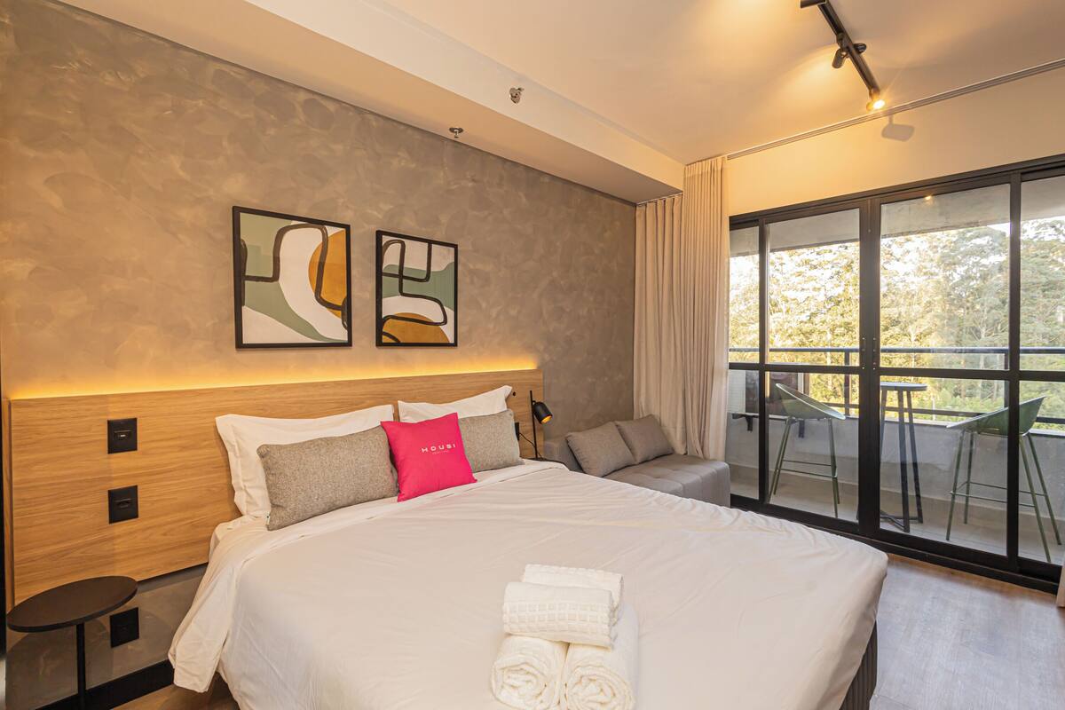Une chambre d’hôtel moderne avec un grand lit, un balcon avec des chaises et des œuvres d’art accrochées au mur.