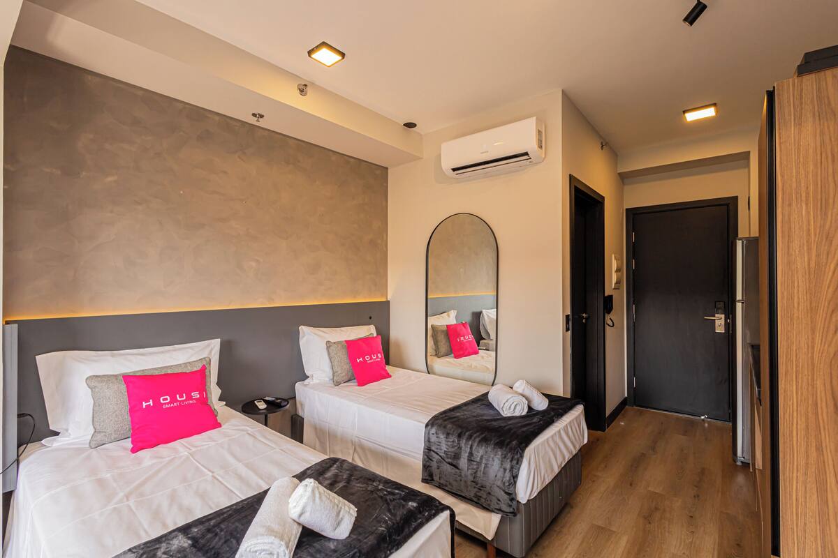 Une chambre d’hôtel avec deux lits, un grand miroir, un appareil de climatisation et une porte en bois.