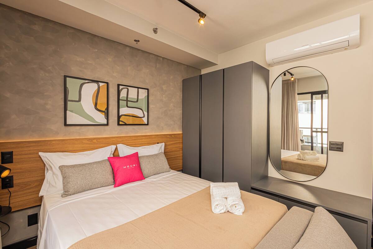 Une chambre d’hôtel avec un lit, un miroir rond, des œuvres d’art au mur et une armoire.