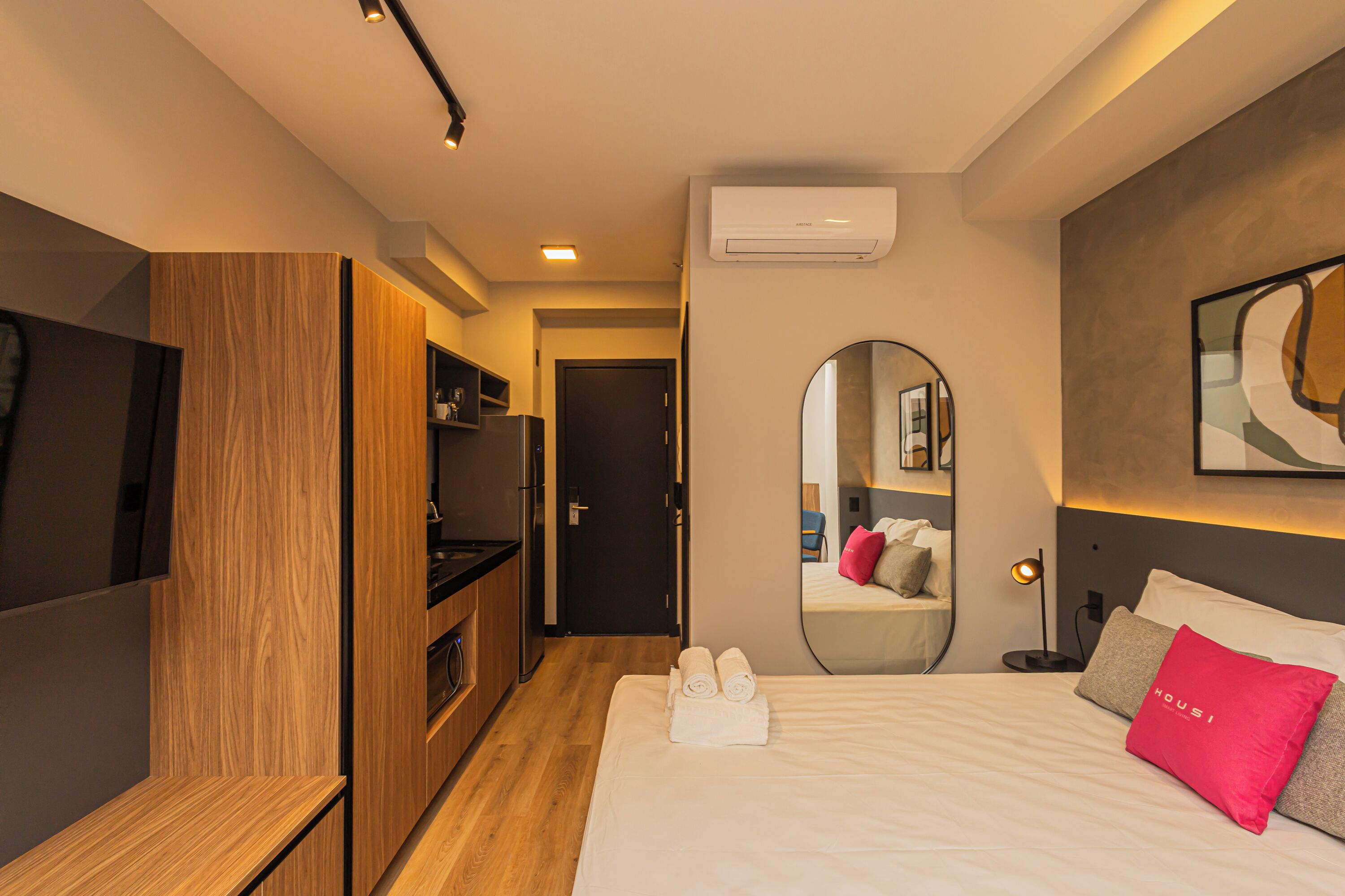 A hotel room with a bed, a TV, a mirror, and a kitchenette.