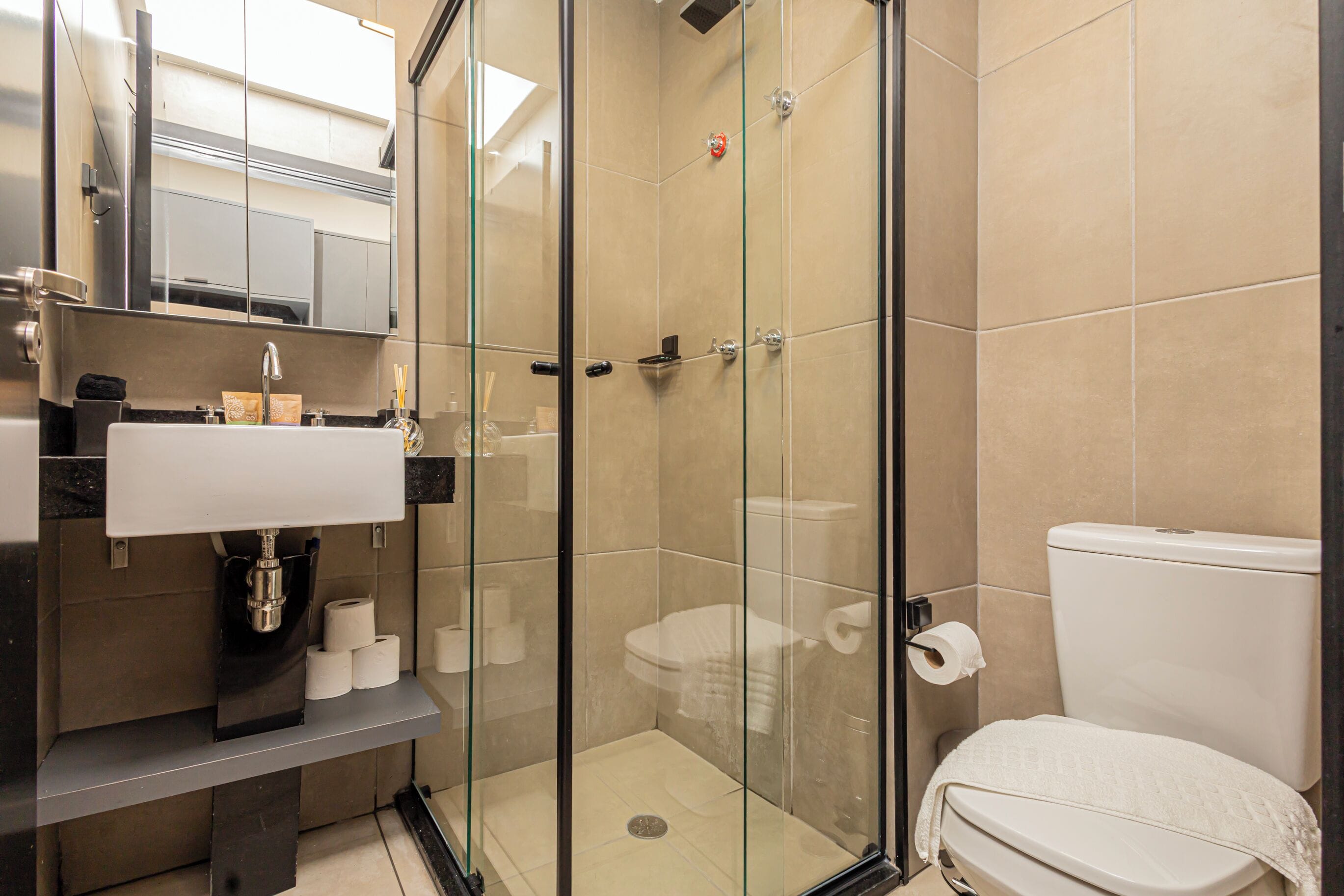 Un baño moderno con ducha de vidrio, lavamanos con espejo e inodoro.