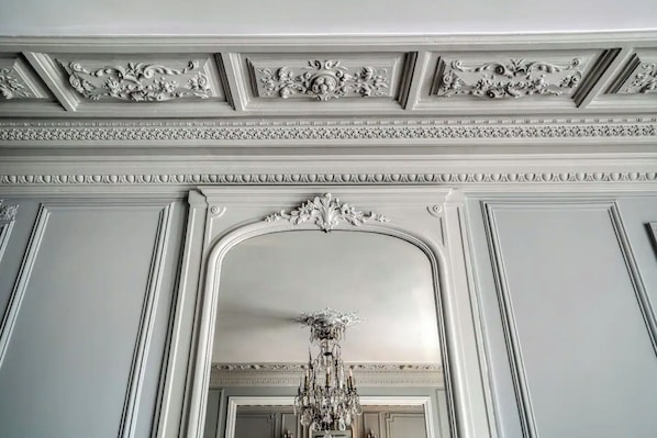 A grand hallway with ornate plaster moldings, a large arched doorway, and a chandelier.