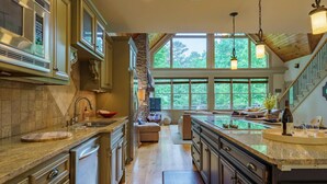 A spacious kitchen with a large island, stone accents, and a view of the outdoors through large windows. - Beautiful Lake Home/Private Dock (Gainesville)