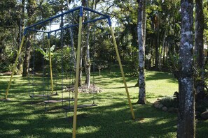 A swing set in a park with grass and trees. - Beautiful House! Enjoy nature and cool off in the pool. (Morretes)