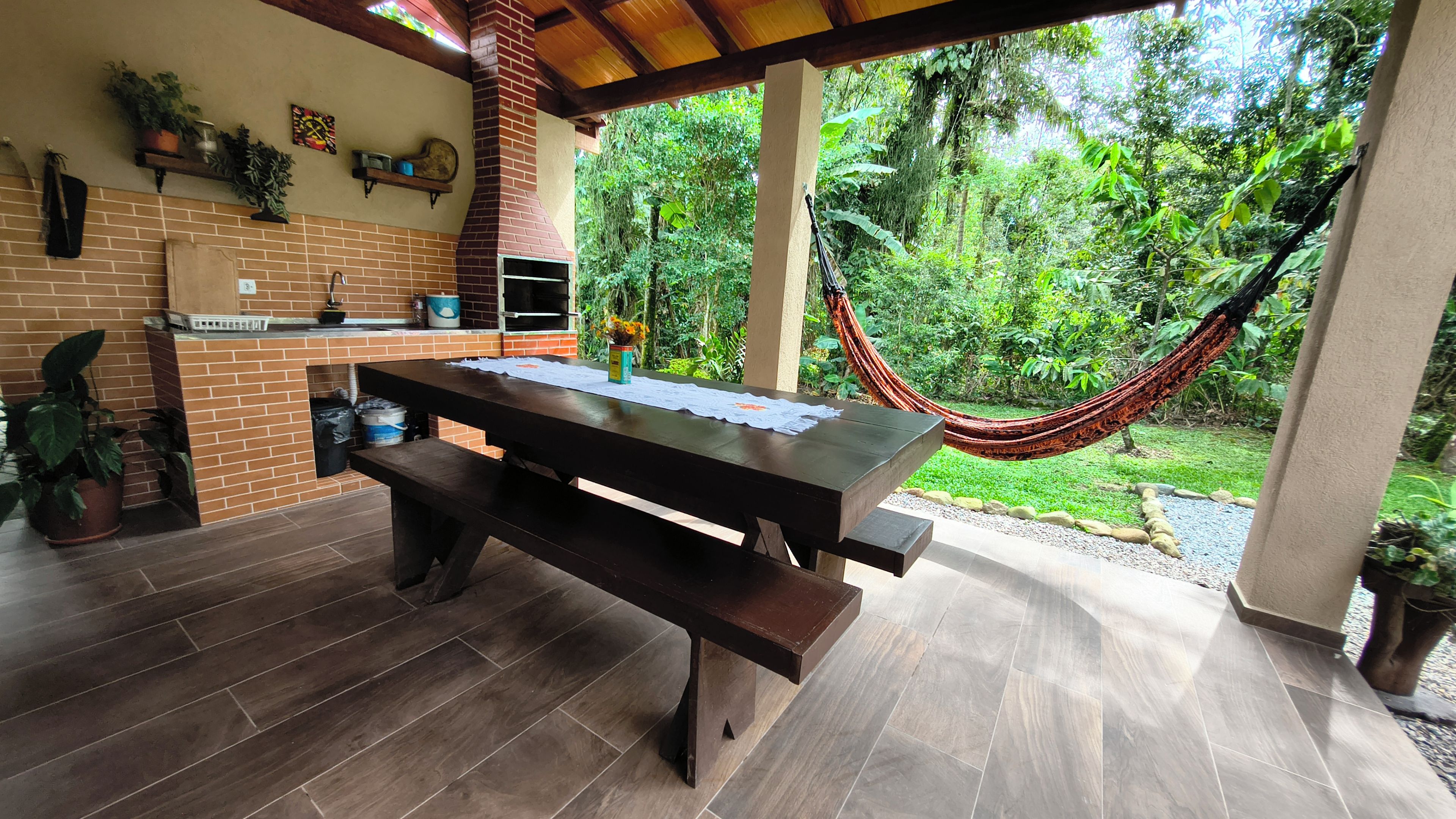 Eine Terrasse im Freien mit Kamin aus Ziegelsteinen, einem Holztisch und einer Hängematte.