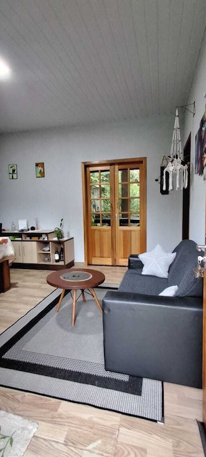 A living room with a sofa, a round coffee table, a wooden cabinet, and a door leading to a balcony.