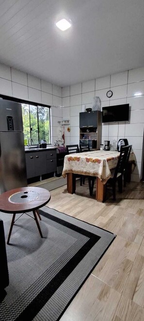 A modern kitchen with a dining area, a refrigerator, a sink, and a television mounted on the wall.