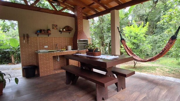 An outdoor patio with a brick barbecue, wooden table, and hammock.