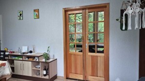 Une pièce comprenant un lit, un bureau en bois avec une plante, une bouteille de vin et une porte donnant sur un paysage verdoyant.