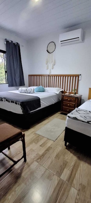 A bedroom with two beds, a wooden headboard, a bedside table, a dresser, a window with curtains, and an air conditioning unit. - Beautiful House! Enjoy nature and cool off in the pool. (Morretes)