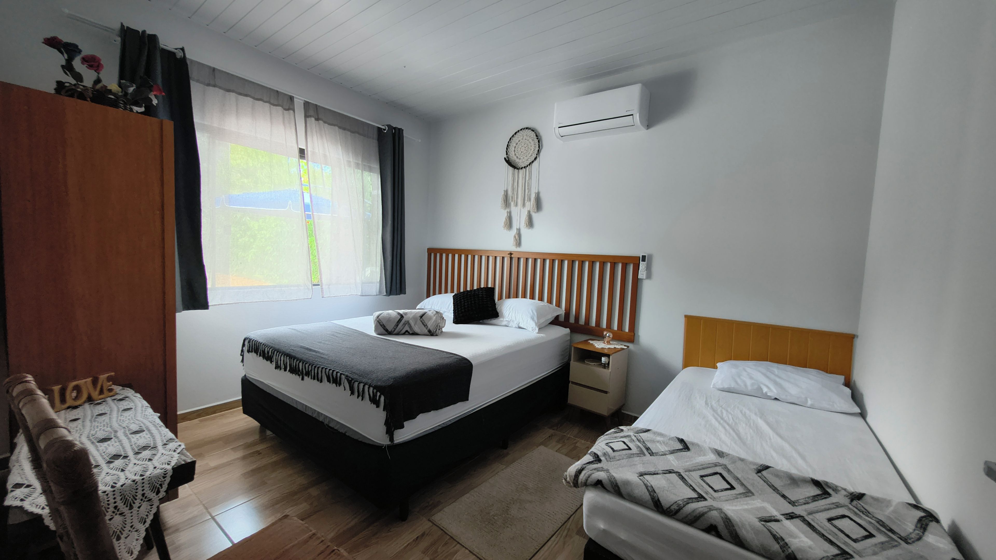 Un dormitorio con cama, mesitas de noche, armario y ventana con cortinas.