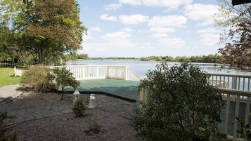 A lakeside deck with a wooden railing, surrounded by trees and shrubs.