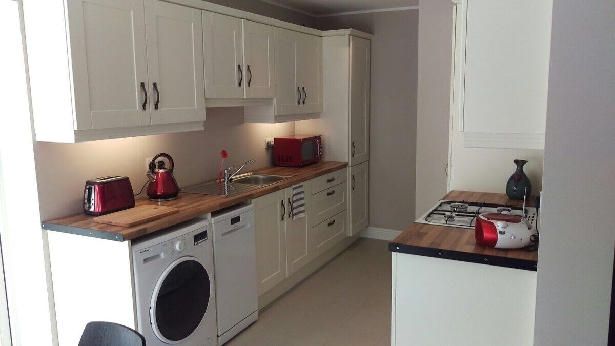 A compact kitchen with white cabinets, a washing machine, a red kettle, and a gas stove.