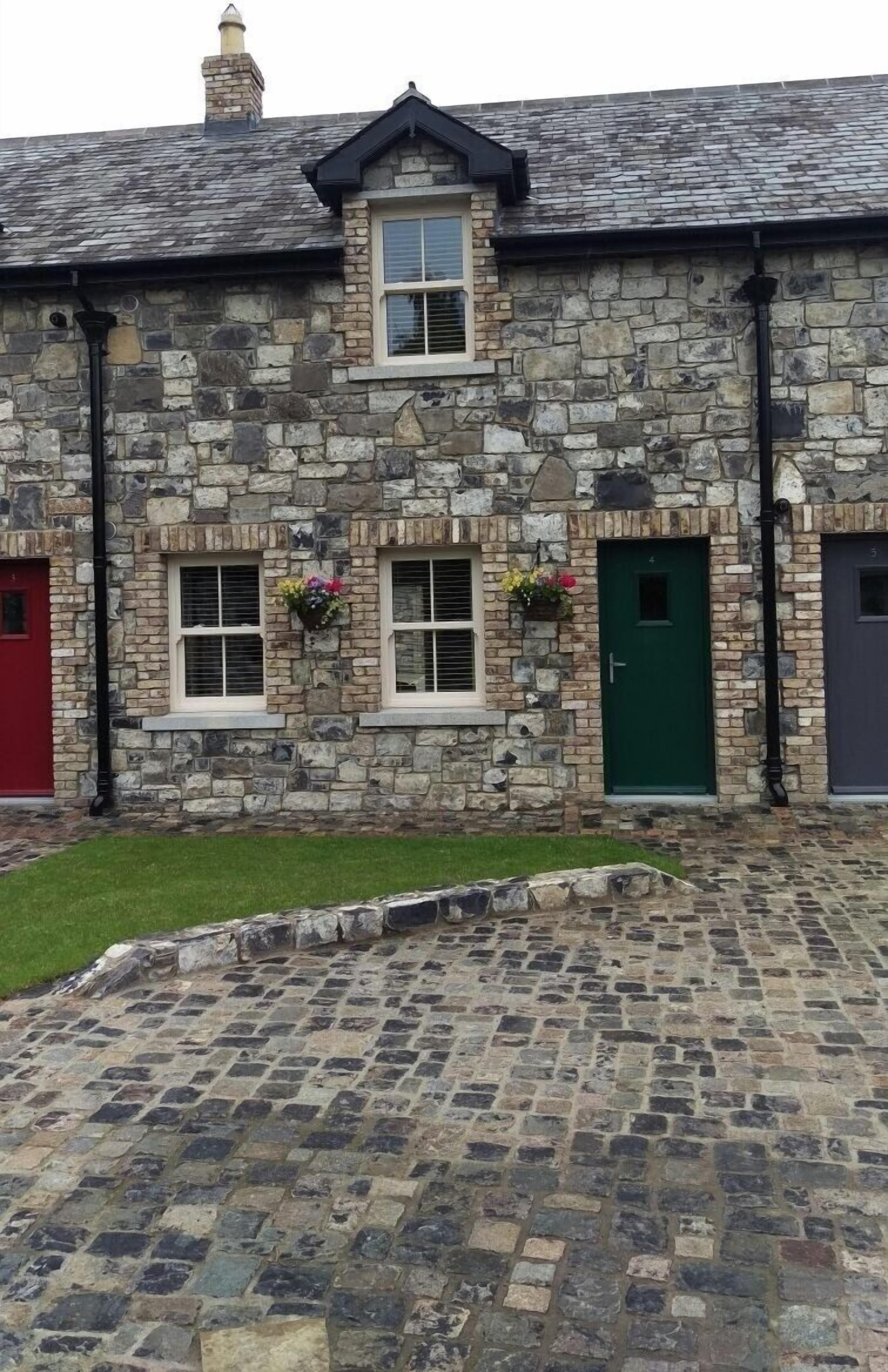 A stone building with three doors, two windows with flower boxes, and a paved driveway.