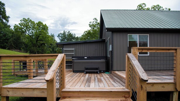 A wooden deck leading to a modern building with a metal roof, surrounded by greenery. - Secluded cabin on 20acres boarding the George Washington National Park (Mathias)