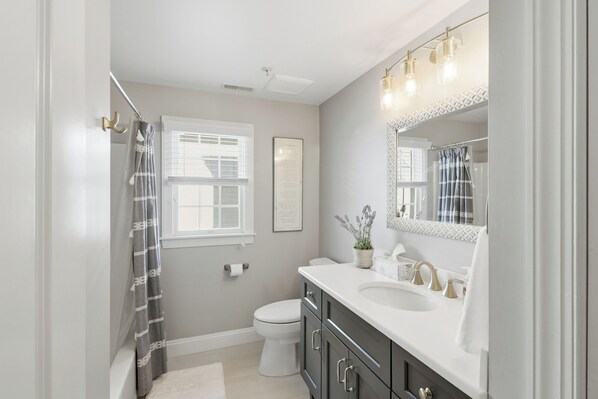 A bathroom with a white toilet, a vanity with a mirror, and a shower curtain.