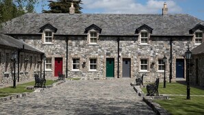A stone building with multiple doors and windows, a paved courtyard, and benches.