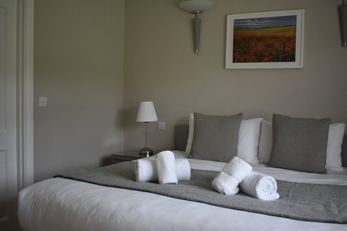 A neatly made bed with rolled towels, a lamp, and a painting on the wall.