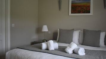 A neatly made bed with rolled towels, a lamp, and a painting on the wall.