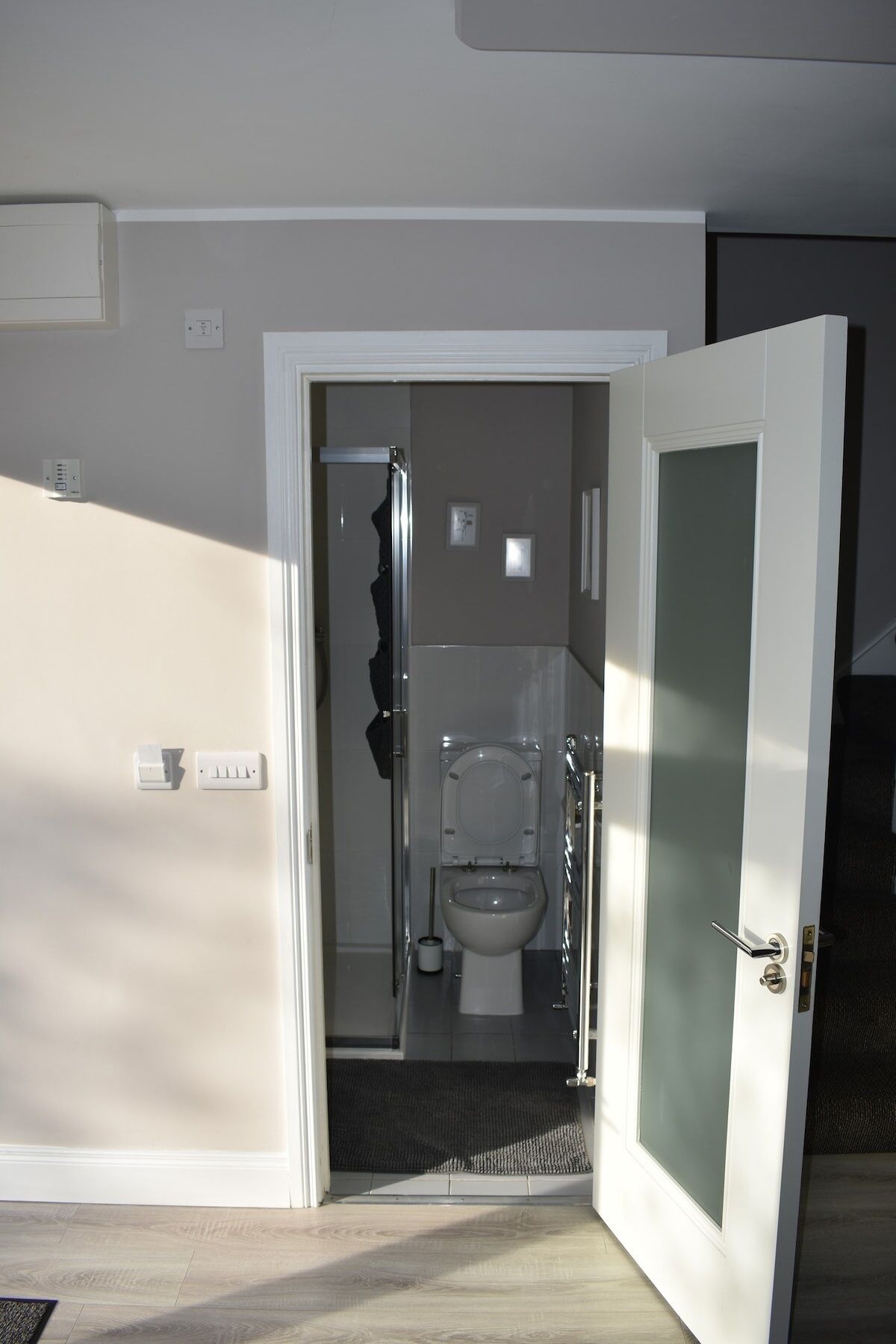 A bathroom with a toilet, a shower, and a door leading to another room.