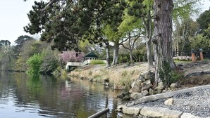 A tranquil riverside setting with a gazebo, trees, and a stone pathway.