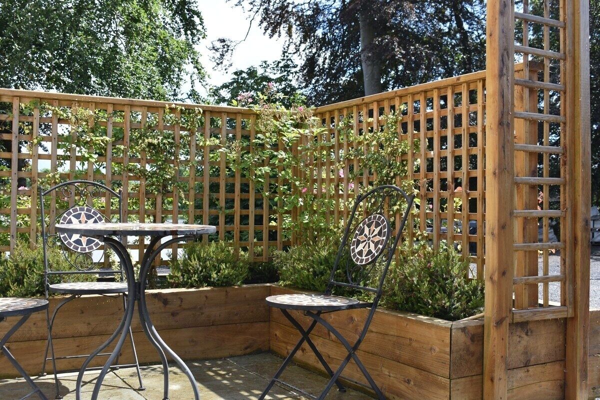 A wooden outdoor seating area with a table and two chairs, surrounded by a wooden fence and plants.