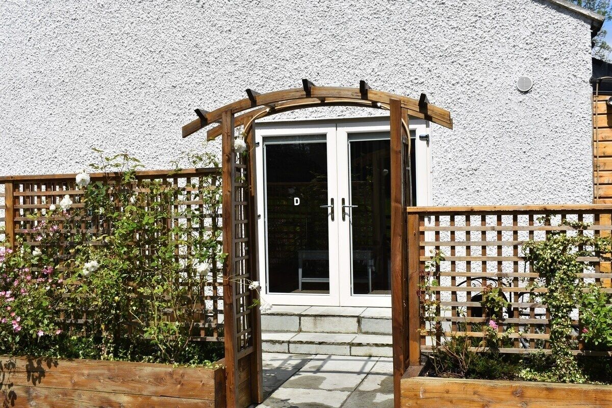 A wooden gate leading to a building with a white textured wall and a door with glass panels.
