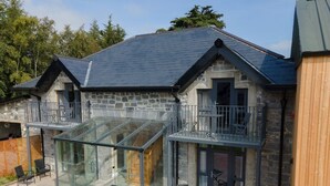 Un bâtiment en pierre doté d’une véranda en verre, d’une terrasse et d’une clôture en bois.