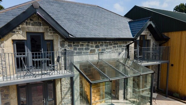 Una casa de piedra con un invernadero de cristal, un balcón y una pared exterior de madera.