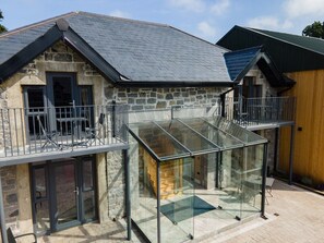 A stone house with a glass conservatory, a balcony, and a wooden exterior wall.