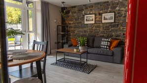 Una sala de estar con pared de piedra, un sofá gris y una mesa de centro de madera.