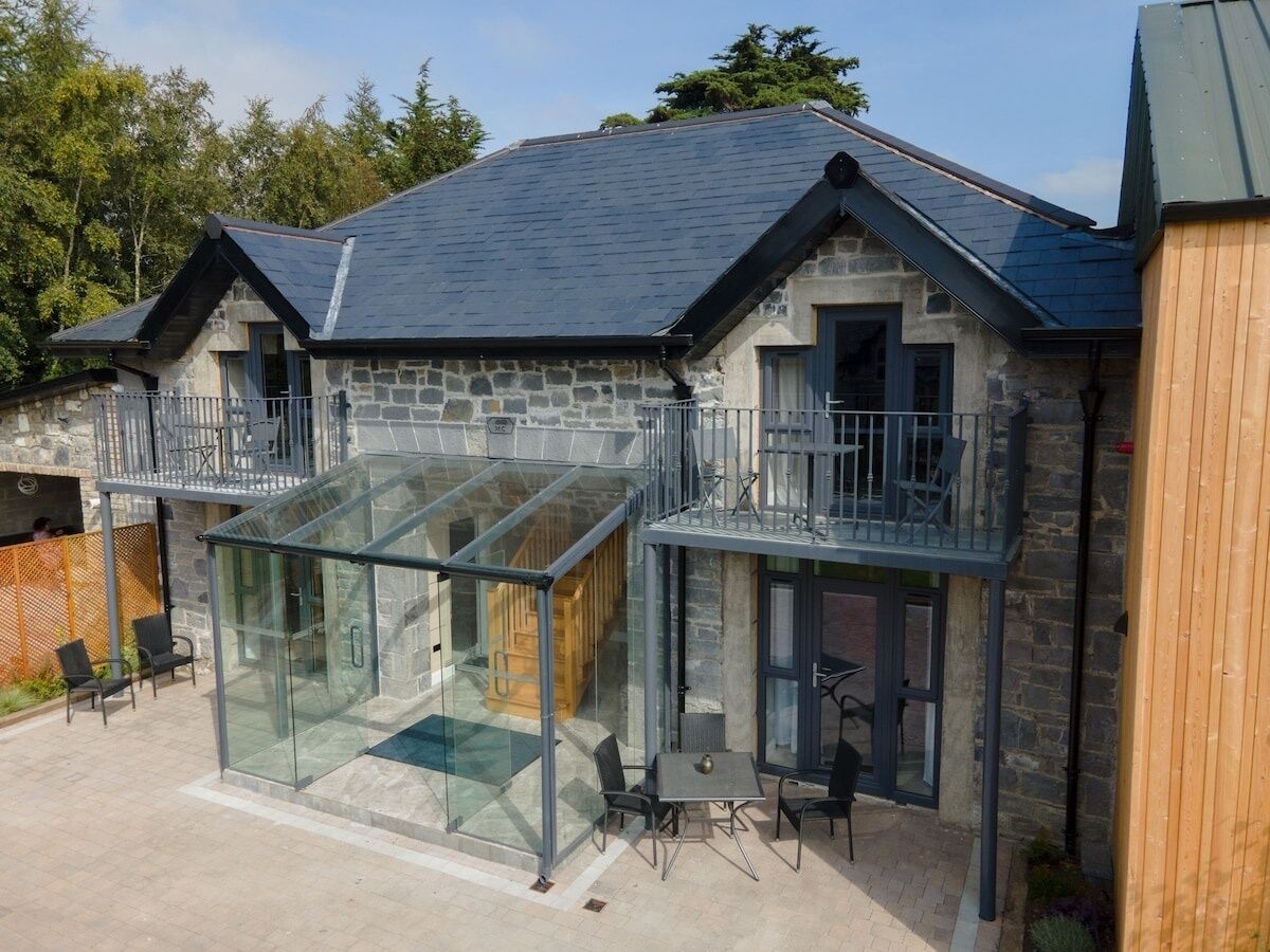 A stone building with a glass conservatory, outdoor seating, and a wooden fence.
