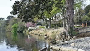 Un río tranquilo con un pabellón, árboles y un muro de piedra.