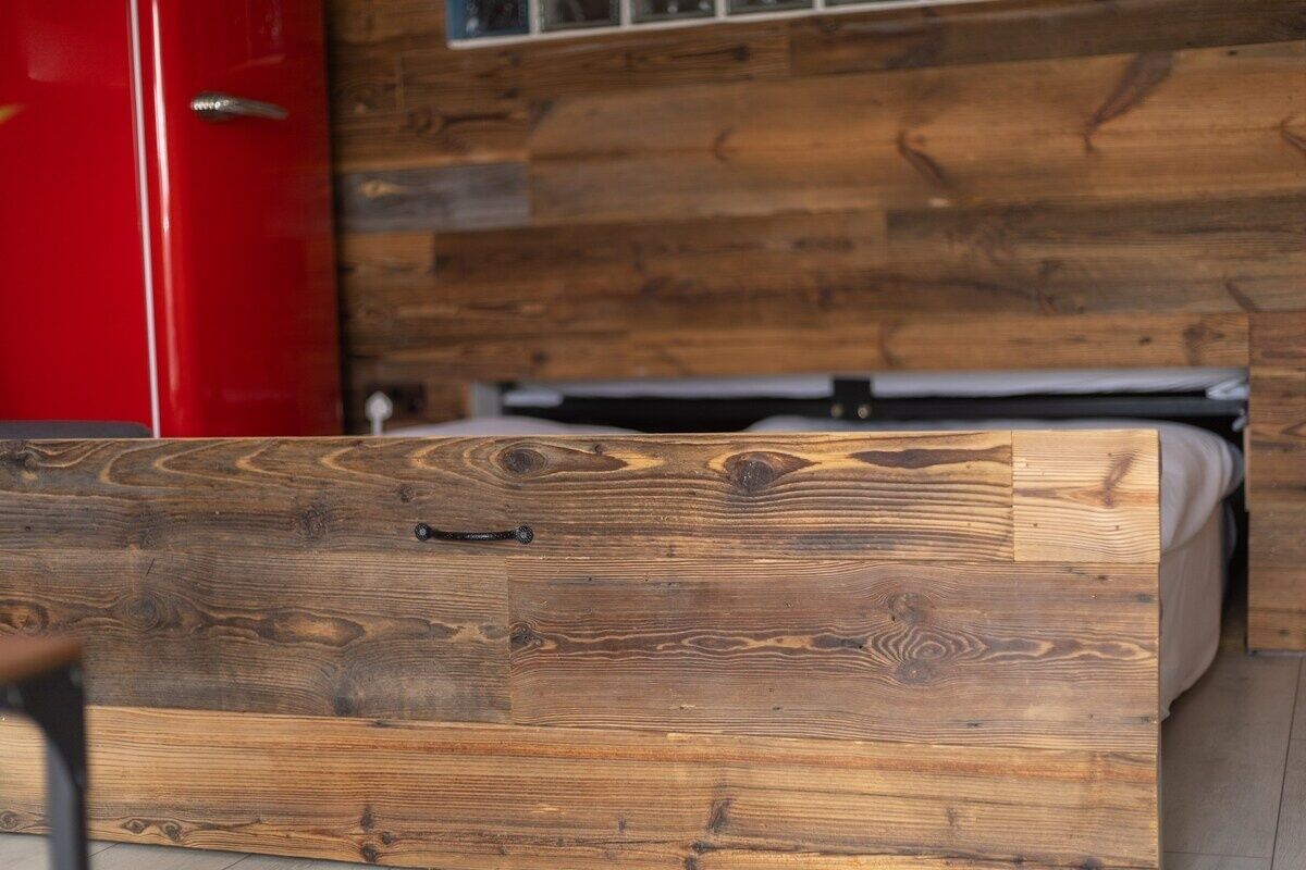 Un aparador de madera con un tirador metálico, un armario rojo y una pared de madera con un ventanal.
