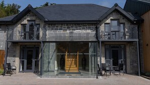 Un bâtiment en pierre doté d’une entrée en verre, d’une terrasse et d’un escalier en bois menant à l’intérieur.