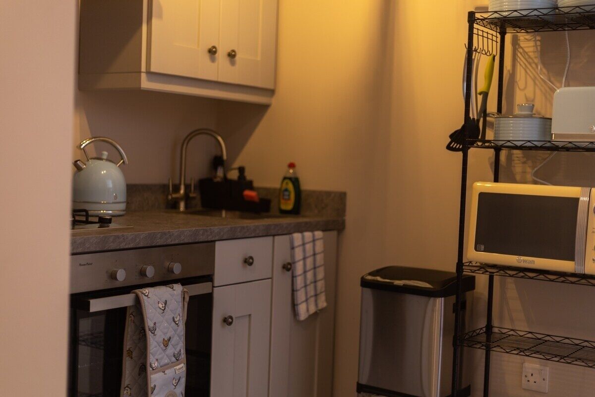 A compact kitchen with a stove, oven, sink, and a microwave on a shelf.