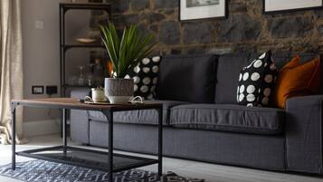 A modern living room with a grey sofa, patterned cushions, a wooden coffee table, and a potted plant.