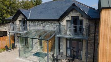 A stone building with a glass conservatory, outdoor seating, and a wooden fence.