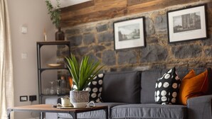 Un salon moderne avec un canapé gris, une table basse en bois et un mur en pierre orné de tableaux encadrés.