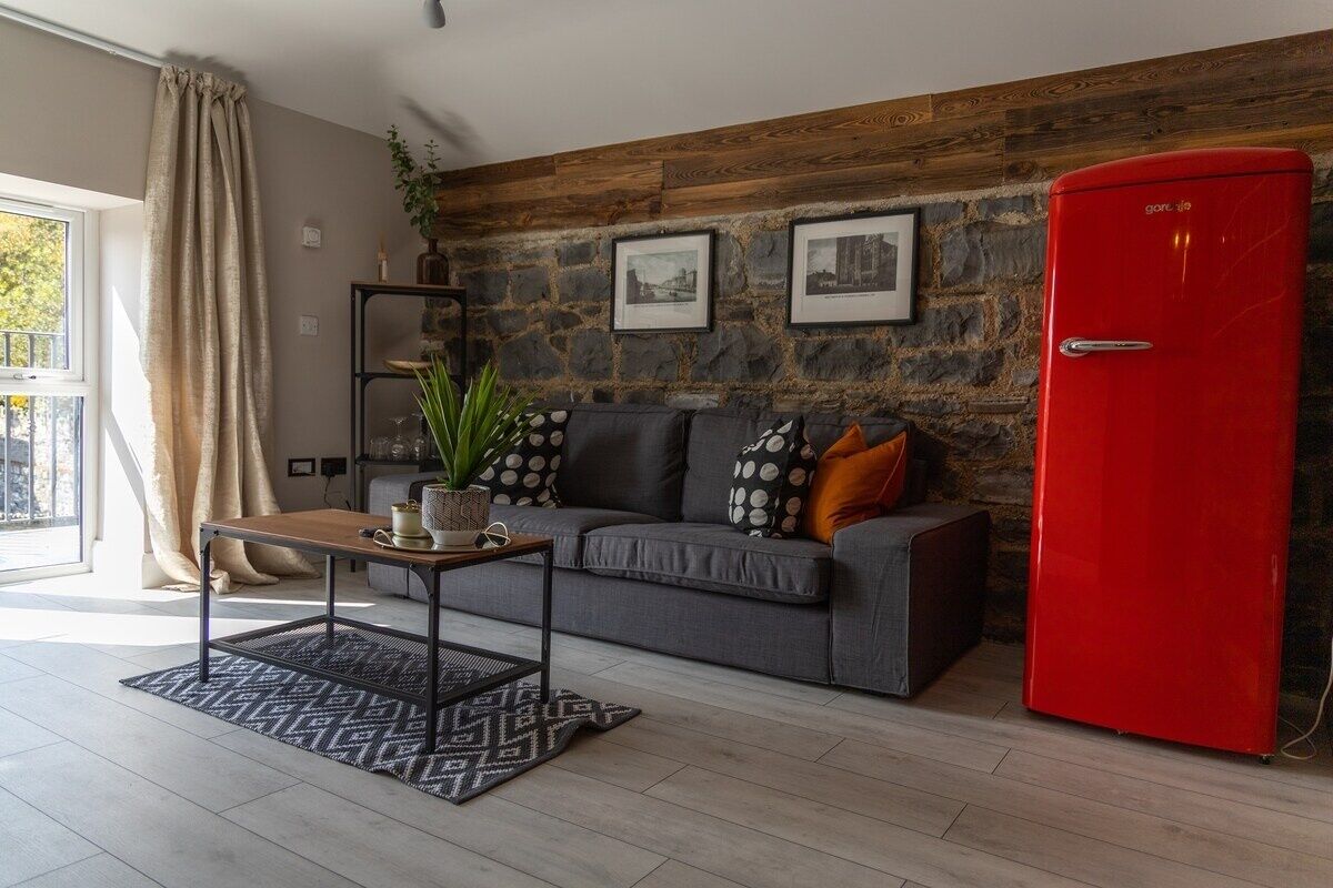 Een moderne woonkamer met een stenen muur, een grijze bank, een rode koelkast en een houten salontafel.