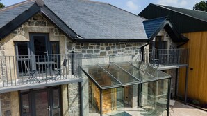 Een stenen gebouw met een glazen conservatorium, een balkon en een houten structuur ernaast.