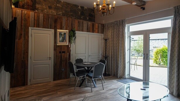 A dining area with a round glass table and four chairs, a chandelier, and a view through a glass door to an outdoor area. - No. 5 The Stone House at Alensgrove (Leixlip)