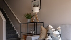 Una sala de estar con un sofá gris, una mesita auxiliar negra con una lámpara y una escalera.