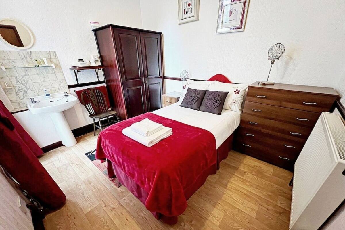 Um quarto com cama, cómoda, guarda-roupa, espelho, lavatório e radiador.