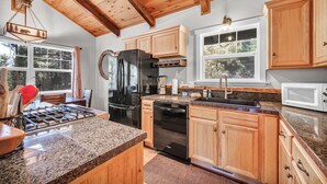 Una cocina con encimeras de granito, gabinetes de madera, un refrigerador negro y una estufa a gas.