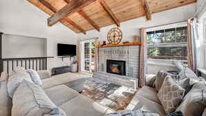Una sala de estar acogedora con chimenea, vigas de madera en el techo, un sofá grande y un televisor.