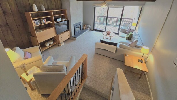 Ein geräumiges Wohnzimmer mit Kamin, einer Holzhockerreolen, einem Fernseher und einem Balkon mit Gartenmöbeln.
