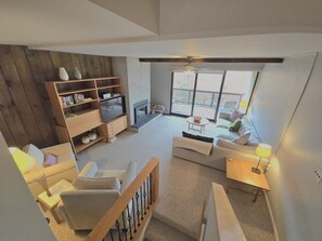 Een ruime woonkamer met een open haard, een houten boekenkast, een televisie en een balkon met tuinmeubilair.